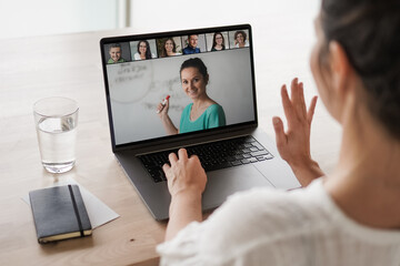 
remote online working woman on her laptop in home office on a desk while talking, flirting and waving hand in a video chat to greet team in a meeting watching video conference or webinar presentation