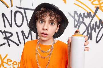 Poster - Surprised teen guy looks shocked at camera holds aerosol bottle spray enjoys creating contemporary art work on street walls wears fashionable clothes leads urban lifestyle. Youth subculture.