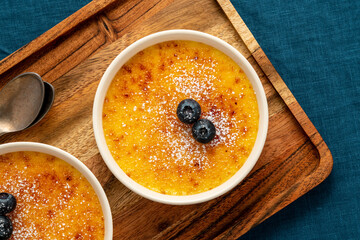 Wall Mural - Creme brulee in ramekin on wooden tray on dark linen tablecloth. Close up french dessert. Burned cream. Spanish crema catalana, rich custard base topped with layer of caramelized sugar. Top view