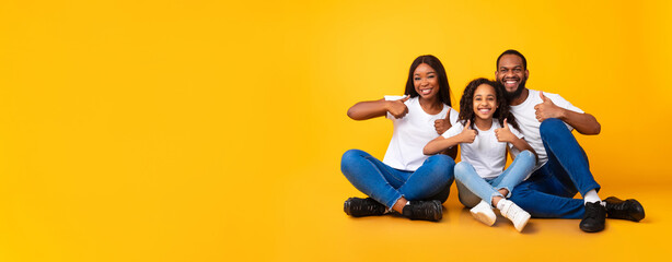 Wall Mural - Happy black family gesturing thumbs up sitting on floor, panorama