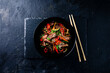 Stir fry soba noodles with beef and vegetables in wok on dark background, Asian noodles with beef WOK in black bowl