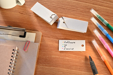Poster - There is a a word card with Software as a Service written on it. They are on the desk along with stationery such as notebooks and colored pens.