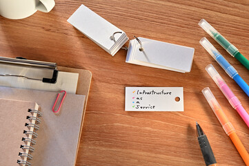 Poster - There is a a word card with Infrastructure as a Service written on it. They are on the desk along with stationery such as notebooks and colored pens.