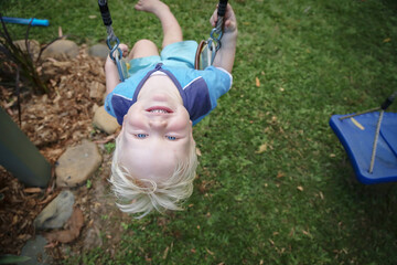 Cute little boy with blonde curly hair playing on backyard swing with big happy smile