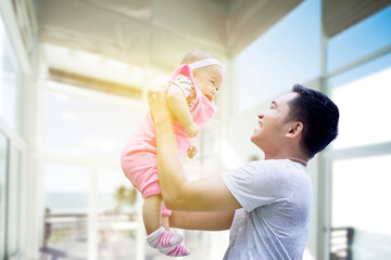 Wall Mural - Happy father lifting his cute baby in living room