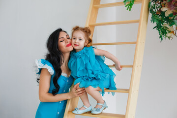 A woman with a little girl in beautiful blue dresses in a bright studio decorated with flowers. Mother and daughter play, hug, have fun.