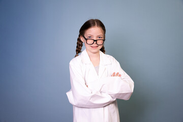 Wall Mural - pretty young girl with black glasses and white work lab coat iis posing in front of blue background