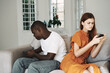 © SHOTPRIME STUDIO - a woman with a mobile phone turned away from an african-looking man on a sofa