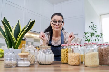 Wall Mural - Storing food in kitchen, woman with jars and containers talking and looking at camera