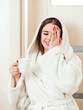Beautiful young woman in a bathrobe with a cup of coffee laughs.