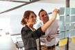 © bnenin - Portrait of a two business people brainstorming using sticky notes on a glass wall.