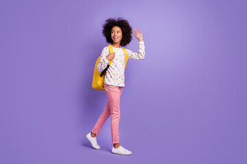 Full body profile side photo of afro american brunette little girl go copyspace wave wear pink trousers isolated on purple color background