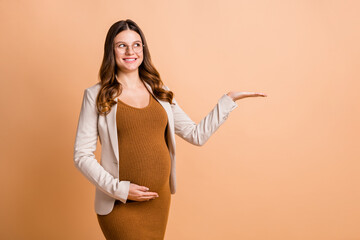 Poster - Portrait of pretty cheerful curious pregnant girl holding on palm copy space decision ad isolated over beige pastel color background