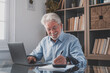 © Daniel - Happy old caucasian businessman smiling working online watching webinar podcast on laptop and learning education course conference calling make notes sit at work desk, elearning concept.