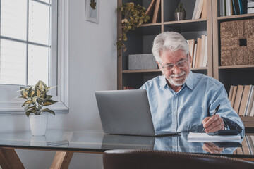 Happy old caucasian businessman smiling working online watching webinar podcast on laptop and learning education course conference calling make notes sit at work desk, elearning concept.