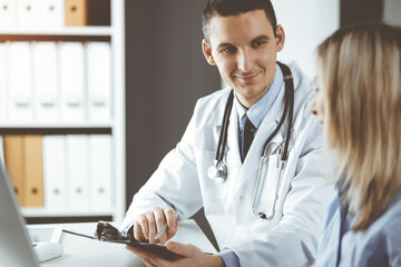 Friendly male doctor and patient woman discussing current health examination while sitting in clinic. Perfect medical service in hospital. Medicine and healthcare concept