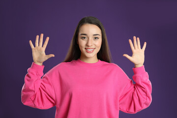 Wall Mural - Woman showing number ten with her hands on purple background