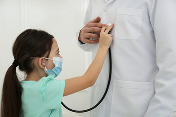 Sticker - Little girl playing with pediatrician during visit in hospital. Patient wearing protective mask