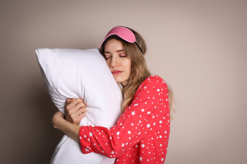 Poster - Young tired woman with sleeping mask and pillow on beige background