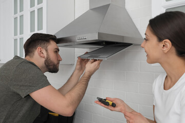 Poster - Man repairing modern cooker hood and woman in kitchen