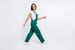 Photo of positive cheerful lady walk go beaming smile wear green overall shoes isolated white color background