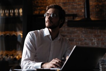 Wall Mural - Handsome young freelancer is having a coffee break and dreaming after working with a laptop at the coffee shop.