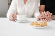 © DragonImages - Close-up image of adult son touching hands of his mature mother when he is visiting her at home and drinking tea with sweet cookies