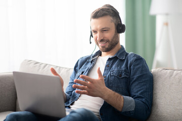 Positive man having video conference, using headset and laptop