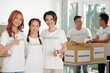 © DragonImages - Portrait of hugging smiling young Asian woman showing thumbs-up when standing in donation center