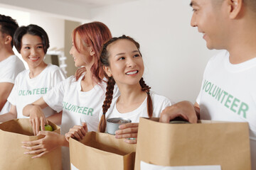 Wall Mural - Pretty young smiling woman volunteering with her friends at donation center and packing groceries for refugees or people in need