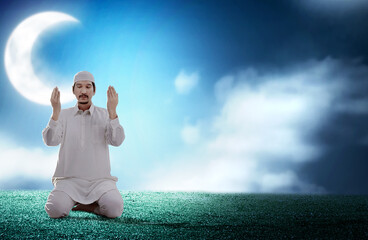 Wall Mural - Asian Muslim man sitting while raised hands and praying