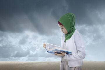 Wall Mural - Asian Muslim woman in a veil standing and reading the Quran