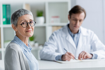 Wall Mural - Mature patient looking at camera near doctor on blurred background