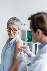 Wall Mural - Mature patient standing near doctor during vaccination