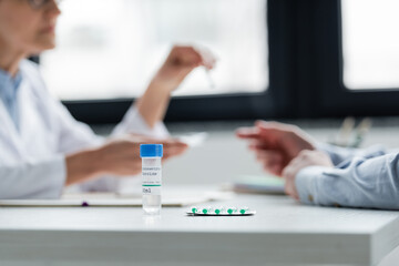 Wall Mural - Cropped view of coronavirus vaccine and pills near doctor and patient on blurred background