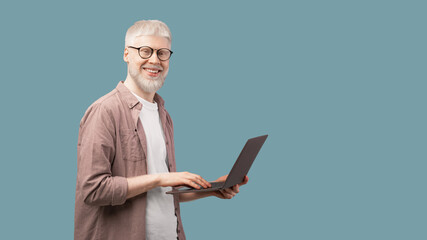 Happy albino man using laptop and looking with smile to camera over turquoise background, panorama with copy space