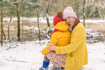 Young mother holding a boy on her lap. Turned back. Winter forest background.