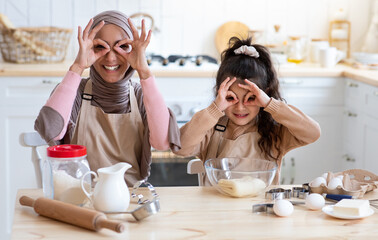 Wall Mural - Cheerful muslim mom and her little daughter fooling together in kitchen