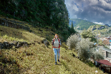 Wall Mural - Young white woman uses walking pole as she climbs hillside near resort town of Fethiye in Turkey.