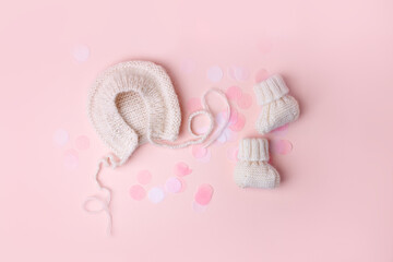 Wall Mural - Bonnet and booties on a pink background. Handmade clothes for a newborn, decorative confetti. Newborn baby gift concept, mom's day, first birthday, first wardrobe, outfit