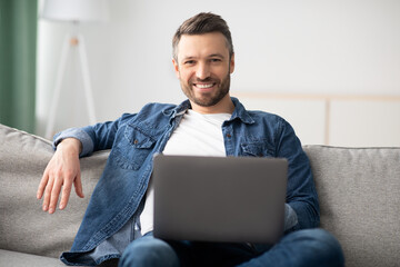 Wall Mural - Cheerful middle-aged man using laptop while resting at home