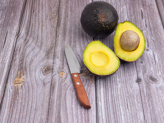 Wall Mural - Top view of the fresh avocado half and knife placed on a wooden table. Organic fruit. Space for text. Concept of healthy fruits and healthcare