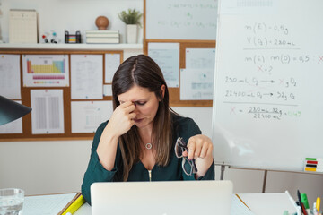 Wall Mural - Young tired female professor having headache.
Teacher holding online class for e-learning students at home during COVID-19 pandemic period. Stressed woman take off glasses feel pain rub closed eyes