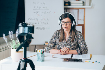 Wall Mural - Teacher recording video tutorial for e-learning class. Female professor working from home teaching online using camera and headset for live streaming to 
physic student studying from home
