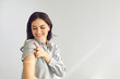 © Studio Romantic - Happy lady shows bandage on her arm after getting flu or Covid-19 vaccine. Woman promoting coronavirus vaccination and immunization campaign on light gray empty blank text copyspace studio background