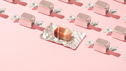 Trendy pattern made of silver wrapped bacon candy on sunny pastel pink background.