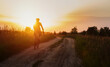 Silhouette of cyclist on a gravel bike riding on a dust trail at sunset.