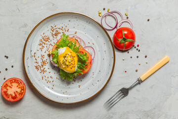 Poached egg sandwich with mustard sauce, tomatoes and onions on a gray plate. eggs Benedict. Overhead, horizontally, with space.