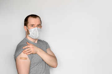 A young adult man wearing a protective face mask shows his arm after vaccination. Theme immunization during pandemic covid-19. Space for text, selective focus