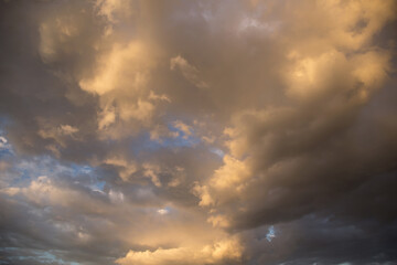 Wall Mural - Epic sunset storm sky. Big white grey cumulus thunderstorm clouds in yellow orange sunlight on blue sky background texture